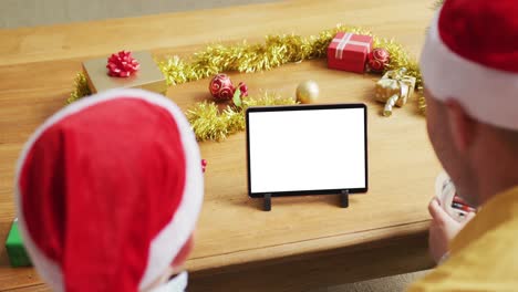 Caucasian-father-with-son-in-santa-hats-making-tablet-christmas-video-call,-copy-space-on-screen