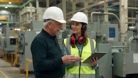 experienced worker guiding colleague with tablet in factory