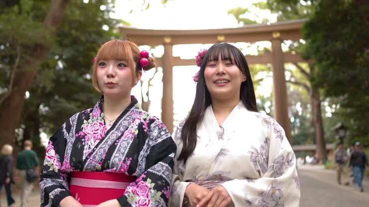 Due donne che indossano kimono tradizionali si inchinano rispettosamente davanti a un grande torii di legno a Tokyo.