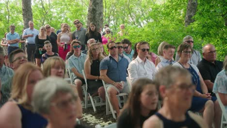 camera pans across guests in summer attire watching the bride and groom