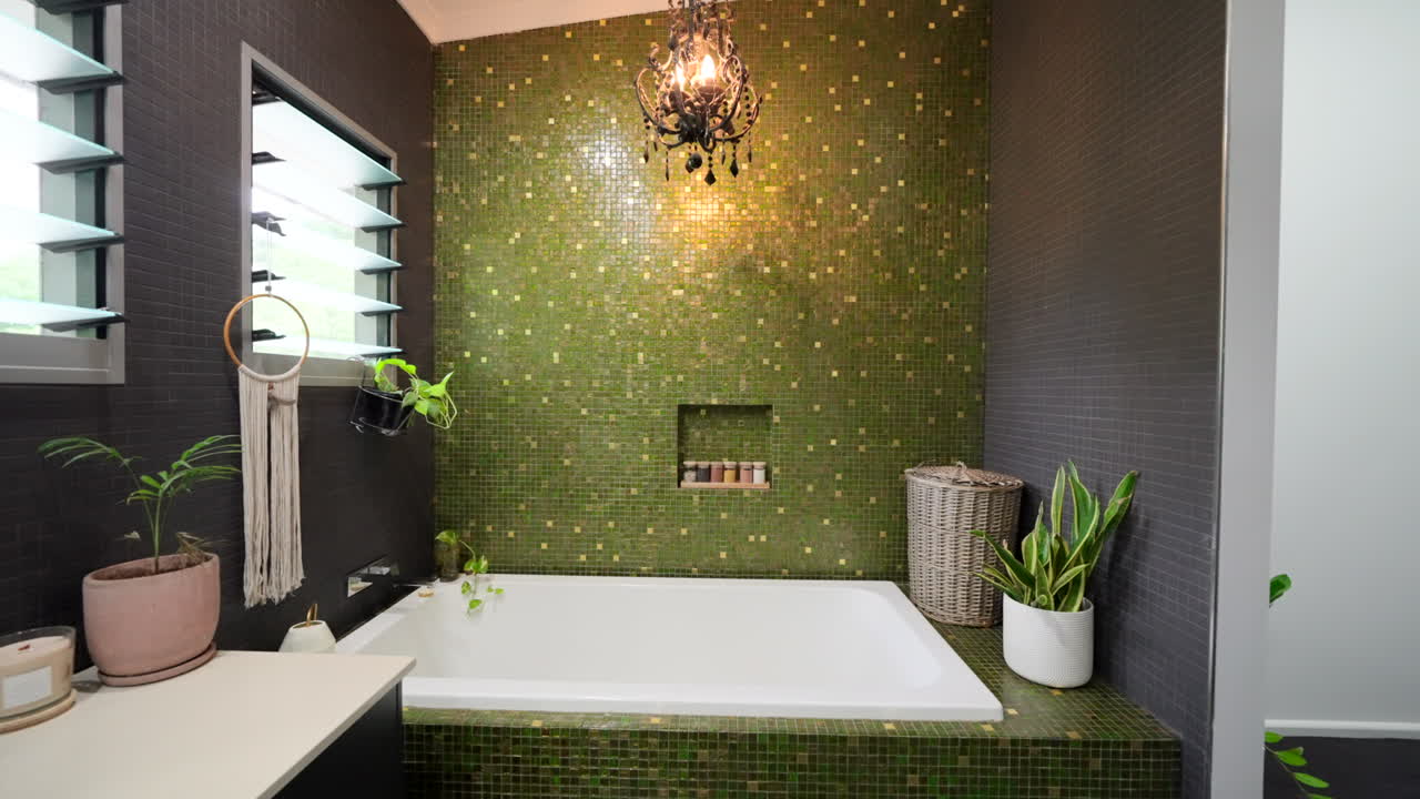 Luxurious Bathroom With Green Feature Tiling and Chandelier Over dark tiled bath, dolly establish