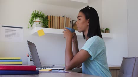 persona de género mixto fluida sentada en un escritorio bebiendo café trabajando desde casa usando una computadora portátil