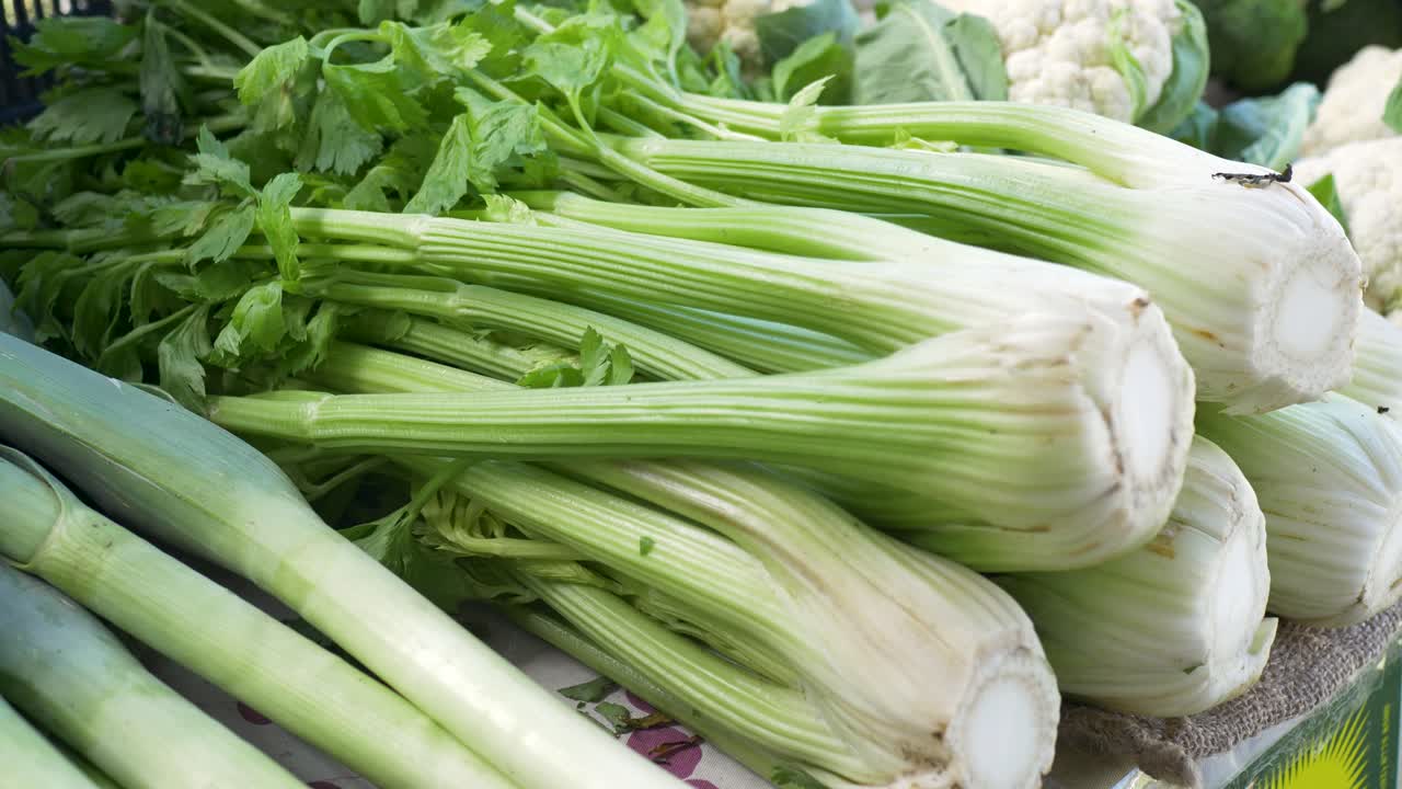Slow motion close up of a bundle of organic celery fresh vegetables with leeks and cauliflower in the background at a farmers market food and produce stall Central Coast Australia agriculture greens
