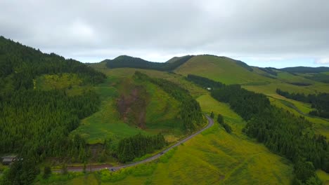 Car-traveling-a-lonely-ascending-road-through-a-vegetated-hill-in-cloudy-landscape