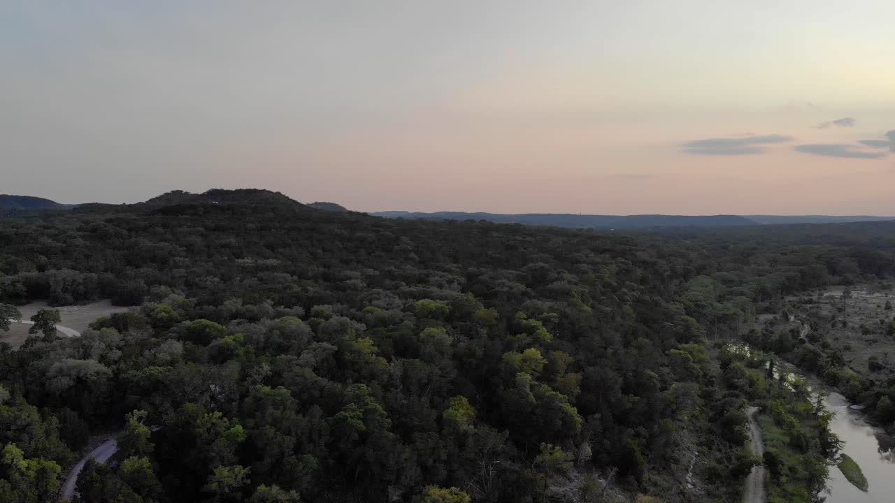 Panoramabeweging naar links, weg van de zonsondergang, toont velden, bomen en een rivier in heuvelachtig gebied.