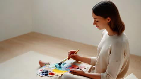 woman painting with a palette and brush on the floor