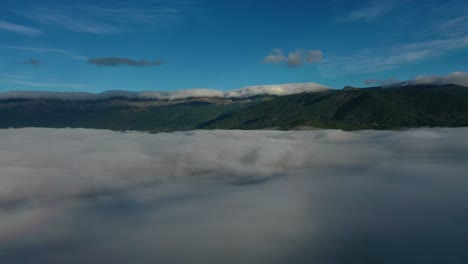 lateral flight with a drone over a sea of clouds visualizing a large mountain system with forests that in turn has a chain of clouds in its peaks at dawn in a valley with a blue sky in avila spain