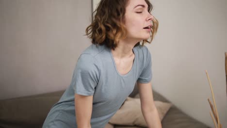 Mujer-Joven-Debilitada-Cayendo-En-Un-Sofá-Después-De-Limpiar,-Sintiéndose-Cansada-Después-De-Lavar-El-Piso-De-Madera.-Exhalando.-Usando-Guantes-De-Goma-Verdes.-Camara-Lenta