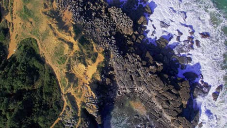 Aerial-top-down-rotation-shot-of-the-rocky-and-grassy-coast-in-Cantabria,-Spain-with-waves-crashing-on-the-coast