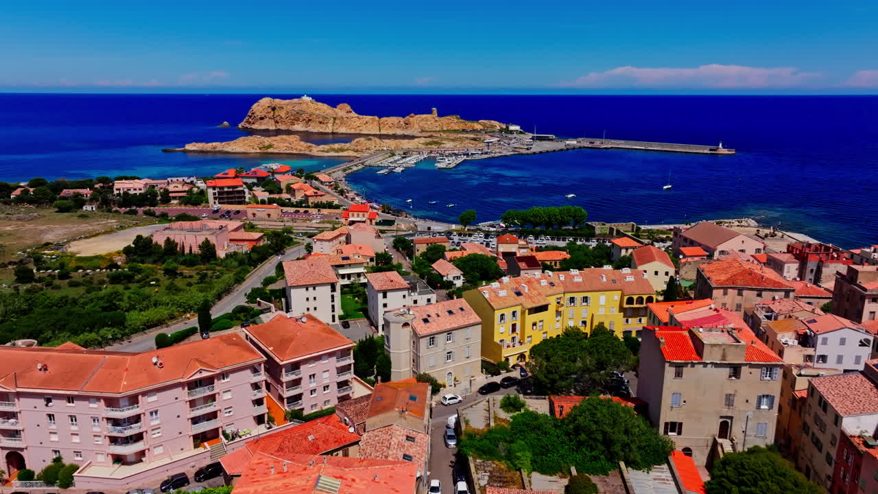 Aerial drone shot over the coastal town Île-Rousse in the Balagne region in Corsica, France. View of the beach and turquoise. Ile de la La Pietra in the background. Summer holidays destination