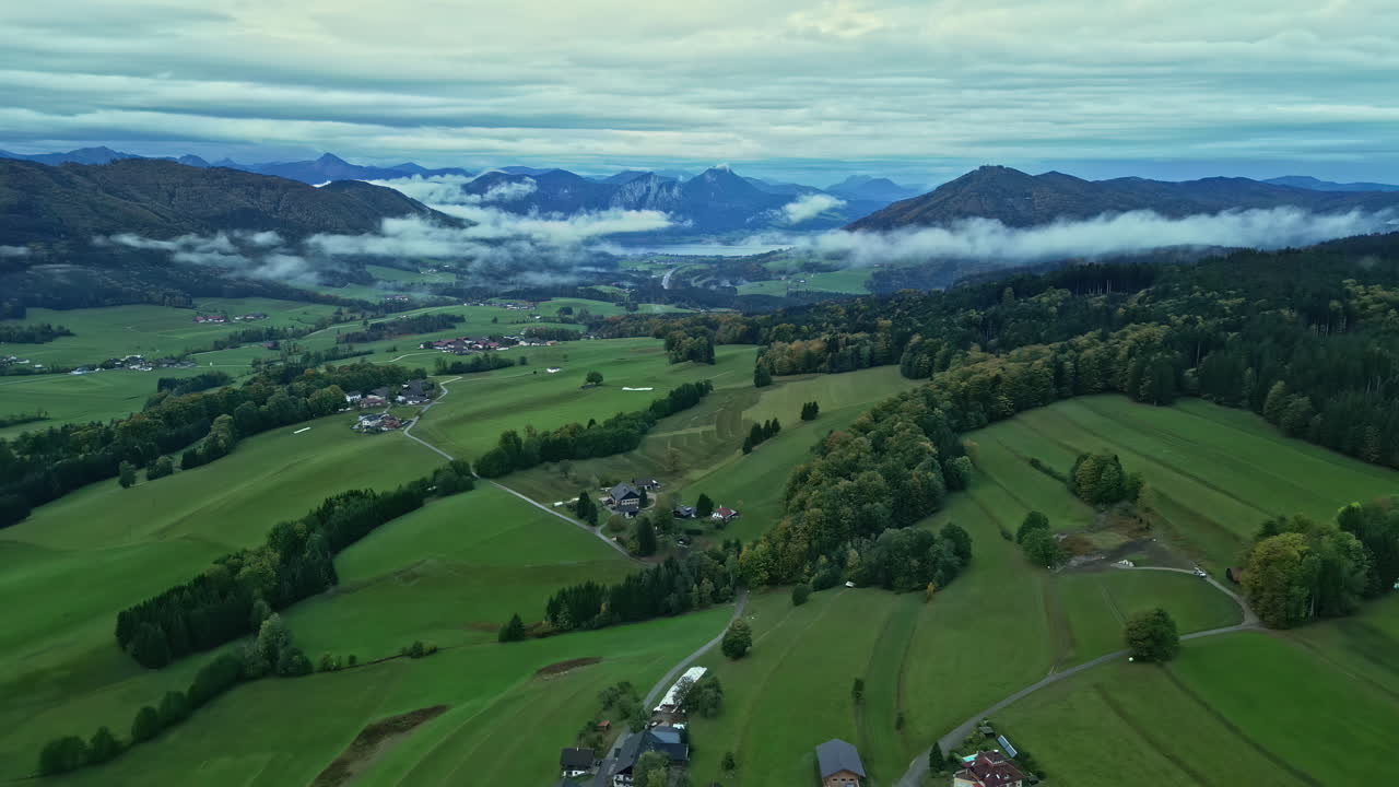 valle verde con casas esparcidas, nubes bajas sobre montañas lejanas al anochecer en austria