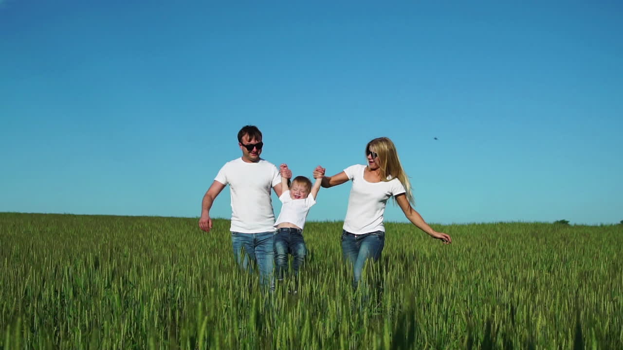 madre e hijo caminan en el campo con clavos en camisetas blancas y vaqueros divertidos balanceándolo en sus manos
