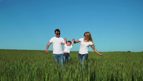Mother-father-and-son-walk-in-the-field-with-spikes-in-white-t-shirts-and-jeans-fun-swinging-it-on-his-hands