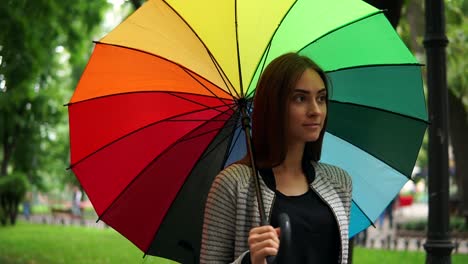 Porträt-Einer-Jungen-Attraktiven-Brünetten-Frau,-Die-An-Einem-Regnerischen-Tag-Im-Stadtpark-Spaziert-Und-Ihren-Bunten-Regenschirm-Dreht