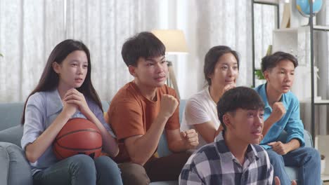 asian teenagers cheering and watching basketball game on tv at home