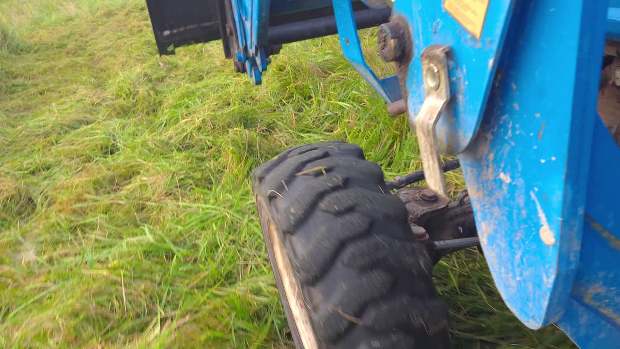tractor compacto conduciendo a través de la hierba vista en el neumático delantero izquierdo
