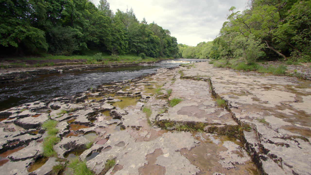 Extra wide shot looking up the river ure with some Swiss cheese limestone holes left of frame at the lower falls at Aysgarth falls, Yorkshire dales