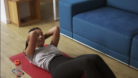 Young-African-American-female-athlete-working-out-in-the-living-room,-doing-abdominal-exercise