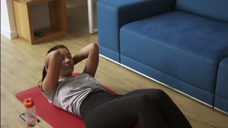 joven atleta afroamericana trabajando en la sala de estar, haciendo ejercicios abdominales