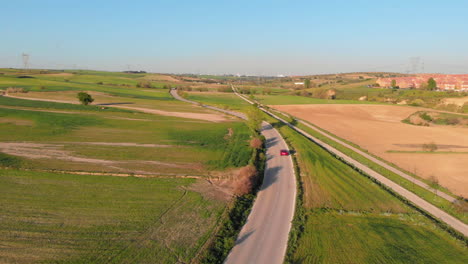aerial shot of a red car driving along a road cutting through agricultural farmland