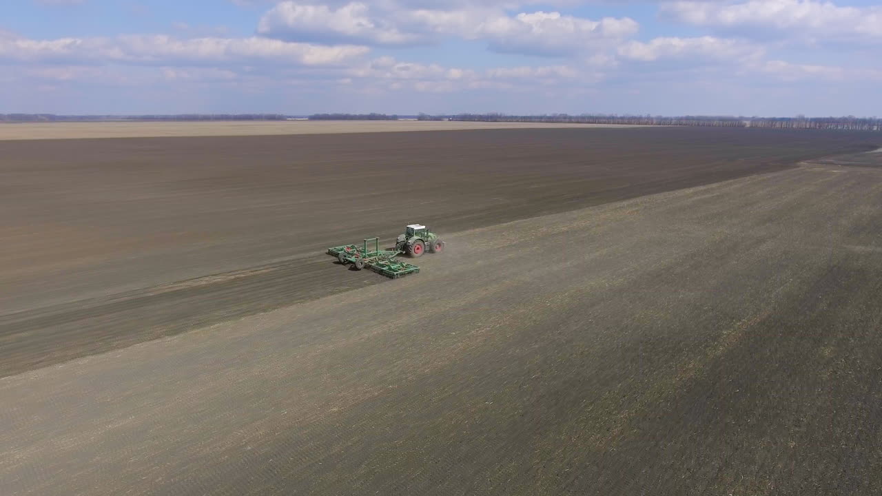 video de seguimiento aéreo: el tractor procesa el suelo en el campo se mueve a lo largo de la diagonal del marco 1