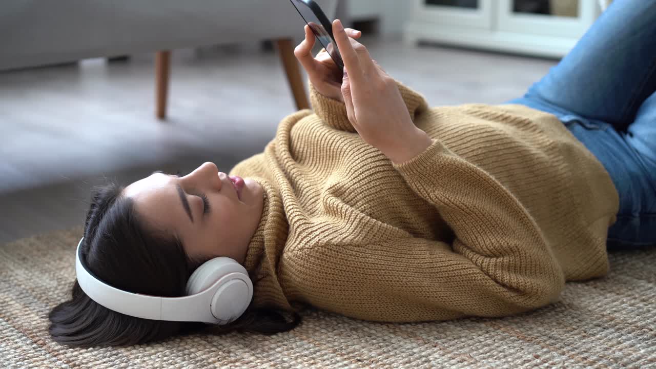 Indian mixed-race woman in headphones listening to favorite music holding phone