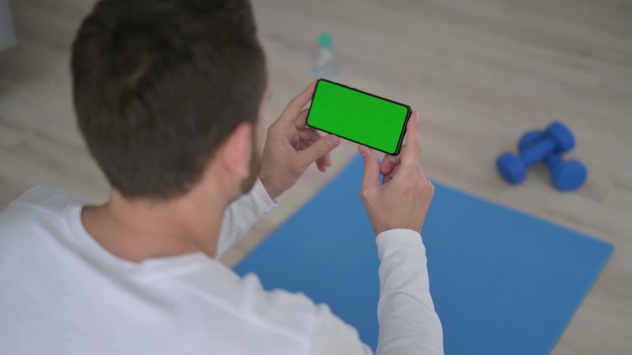 Rear View of Man Looking at Smartphone with Chroma Key Screen on Yoga Mat