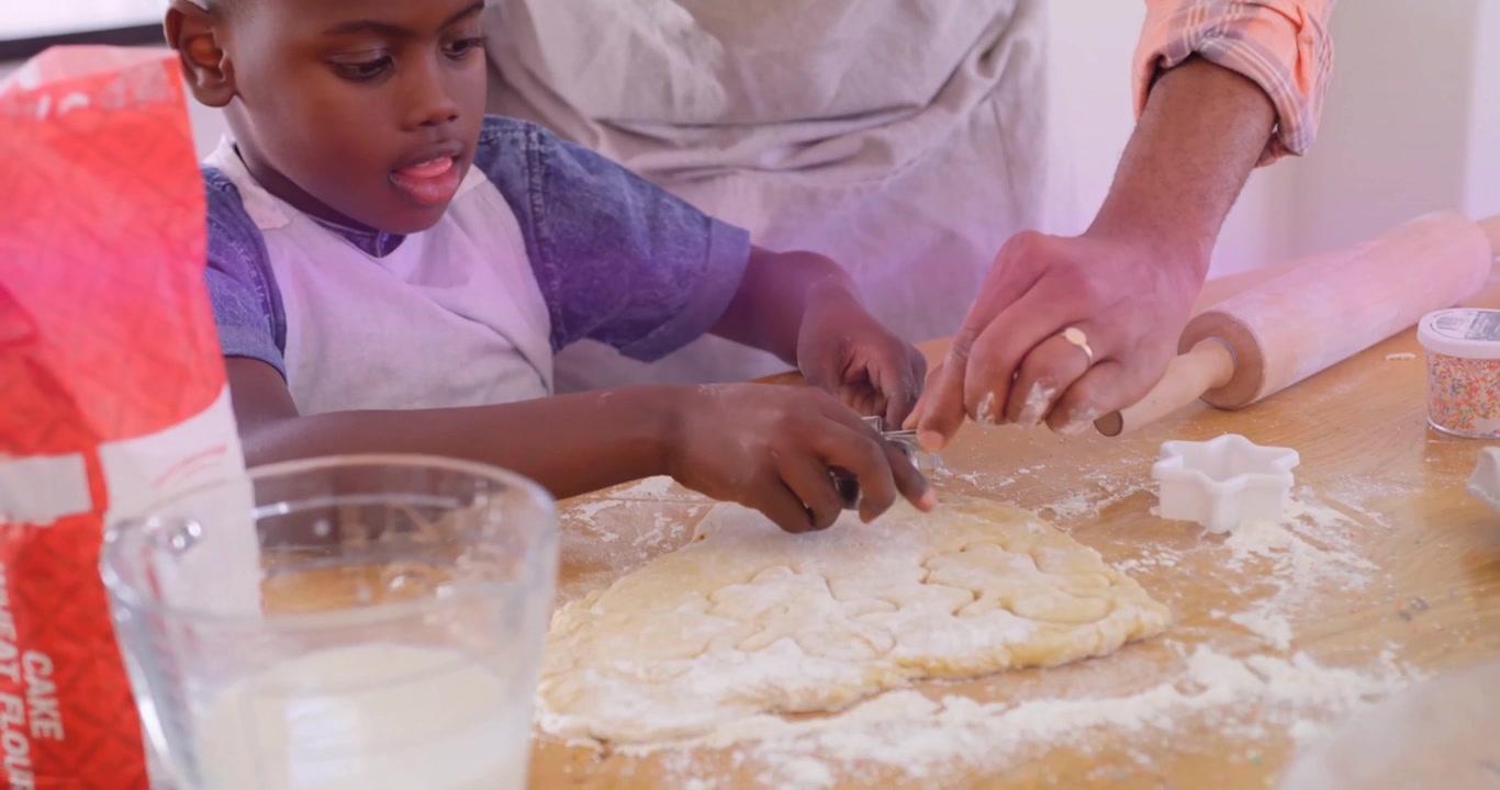 Father and son baking at wood kitchen counter, featuring animated flour icons and cookie shapes