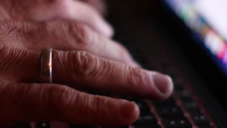 close-up view of a man's hands typing on a laptop backlit by the screen