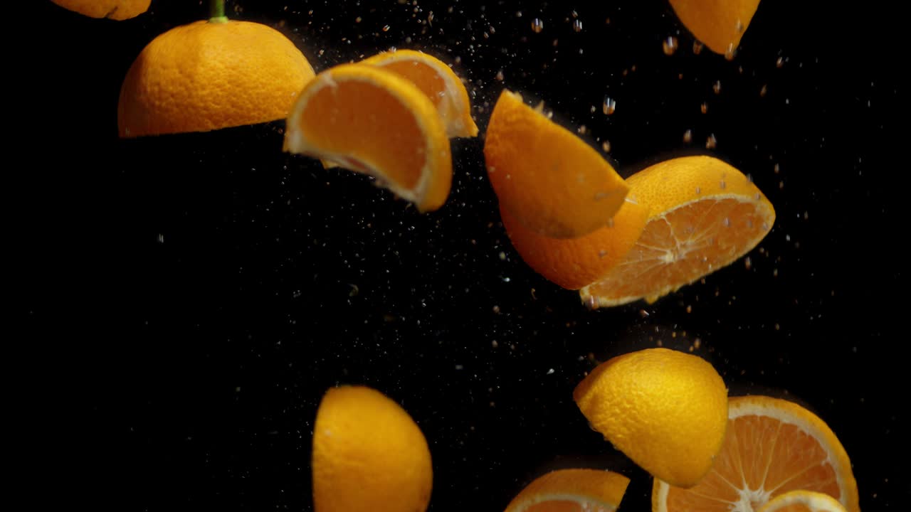Slices of tangerines fall under water with air bubbles.