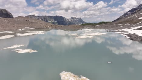 Tranquilo-Lago-Alpino-Con-Bancos-De-Nieve-Flotantes-Y-Montañas-Distantes-En-Klausenpass,-Suiza