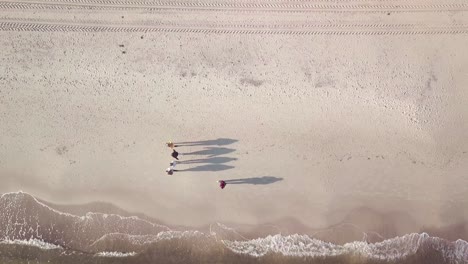 drone shot from the sea to the shore, downward view. camera following the movement of medium waves until it reaches group of people having a early walk on the beach.