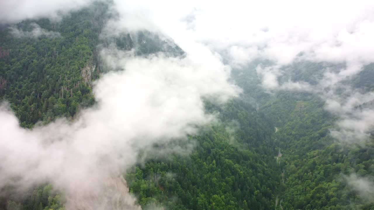 Clouds lying of a mountain forest area of Southern France. Drone footage rotates to the left focusing on a mountain peak with think white clouds over it then continues to the surrounding area