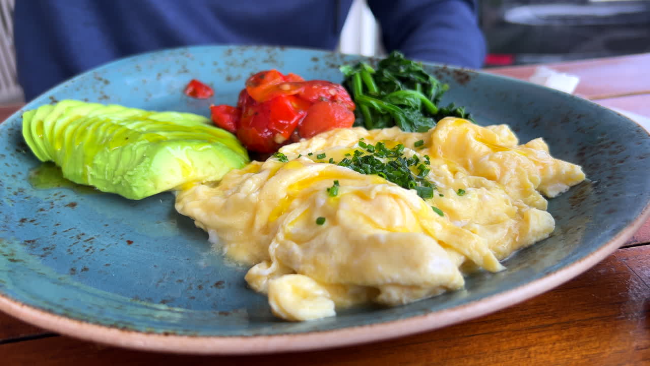 아보카도, 토마토, 시금치를 곁들인 스크램블 에그 위에 엑스트라 버진 올리브 오일을 붓고, 스페인의 건강한 지중해식 아침 식사, 4k 샷
