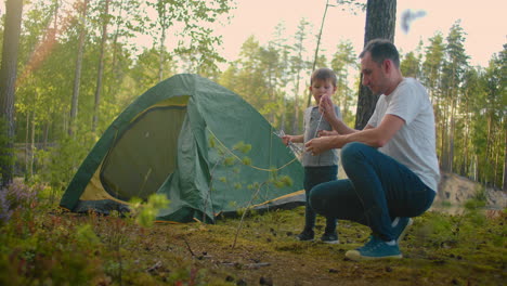 the boy helps his father to set up and assemble a tent in the forest. teaching children and travelling together in a tent camp