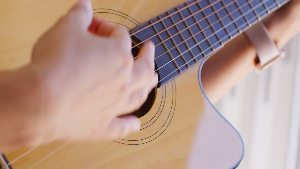 Guitarist hands beside bright window, moving across guitar, plucking and strumming while practicing