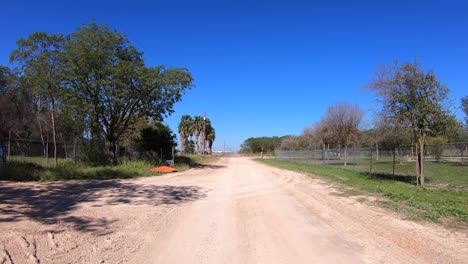 pov driving on a graveled road past a chain link fence and palm trees in southern texas