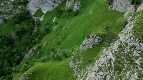 Grassy-hillside-below-white-grey-rocky-cliffs-of-vietnam,-aerial-overview