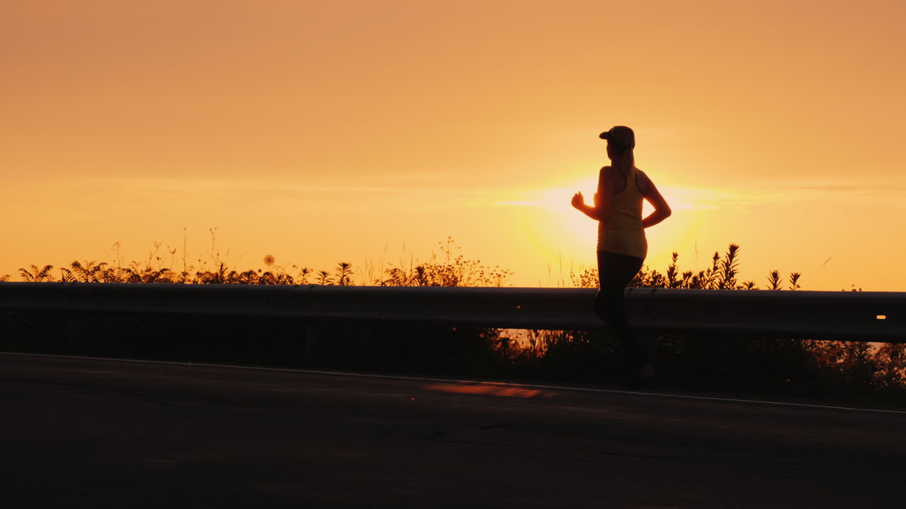 silueta de una joven mujer activa trotando por una carretera cerca del mar al atardecer