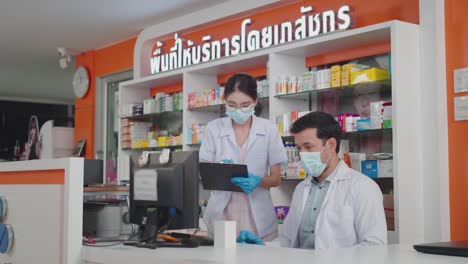 two pharmacists wearing a protective hygienic mask and glove check stock medicine on a computer.