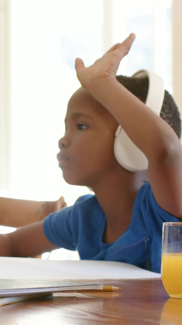 Vertical video: Answering boy in blue shirt white headset raising hand after prompt at home, papers