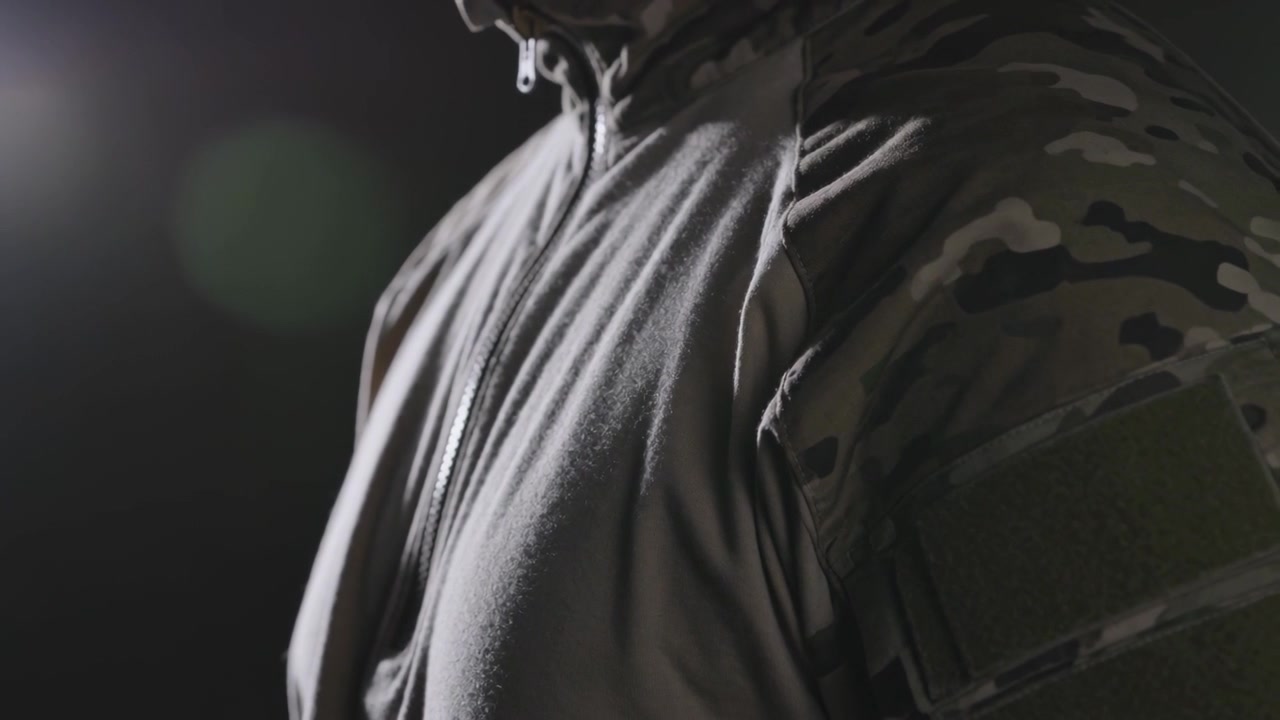 Studio light causing man breathing and tilting collar showcasing camo sleeve velcro patch on hoodie