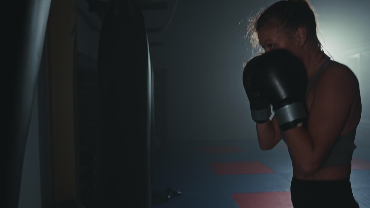 Donna determinata che si allena con un sacco da boxe in una palestra buia