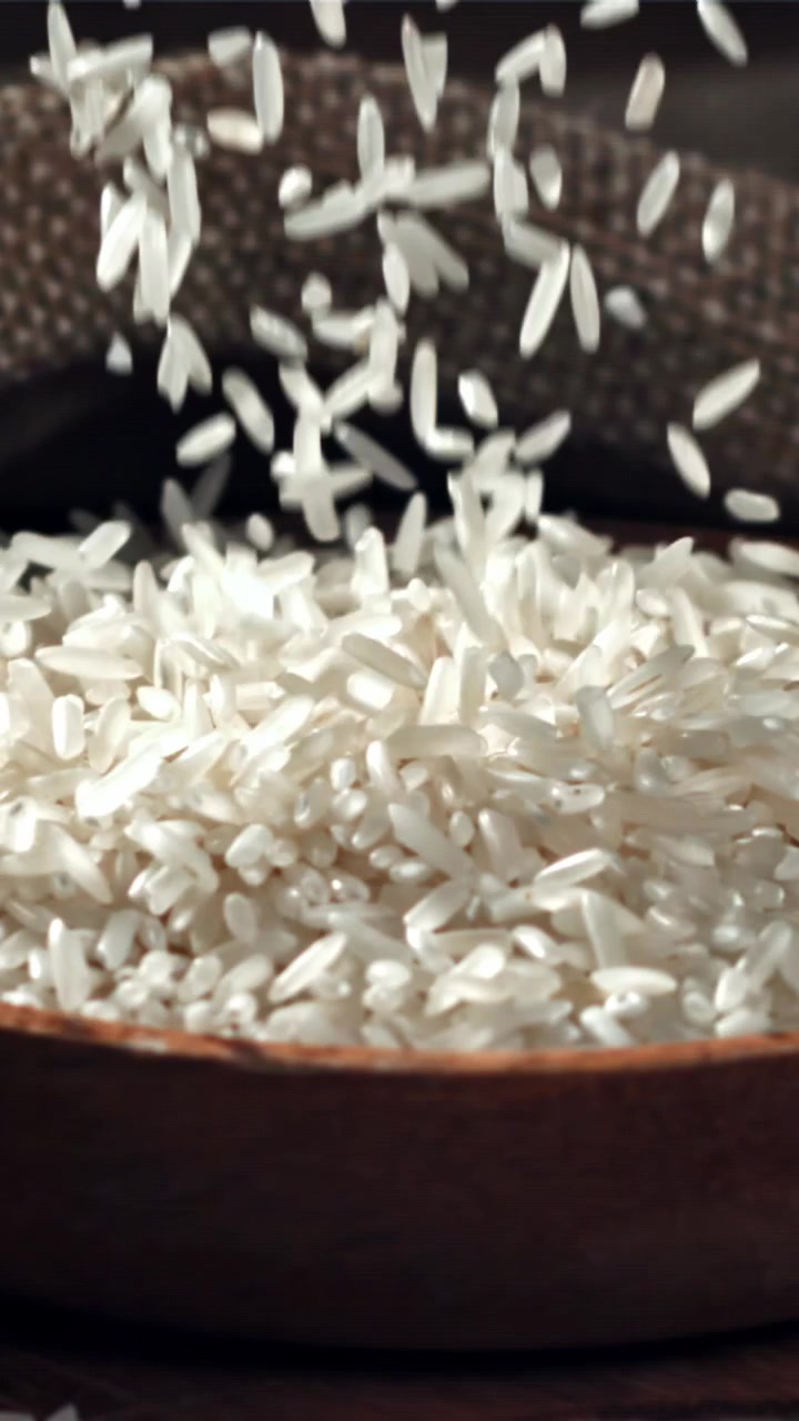 Chicchi di riso bianco che cadono in una ciotola di legno al rallentatore