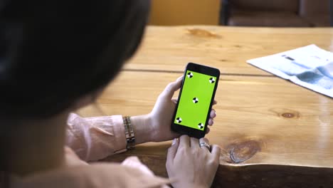 woman holding phone with green screen on wooden table