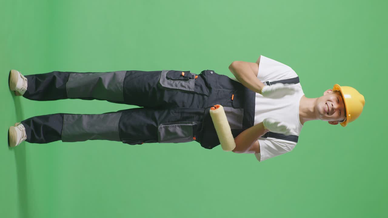 Full Body Of Asian Man Painter Wearing Safety Helmet Smiling And Clapping His Hands While Standing In The Green Screen Background Studio