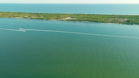 arial view of people riding or driving hydrocycles near playa flecha nueva umbria - spit separating piedras river from atlantic ocean daytime on sunny day, huelva, andalusia, spain