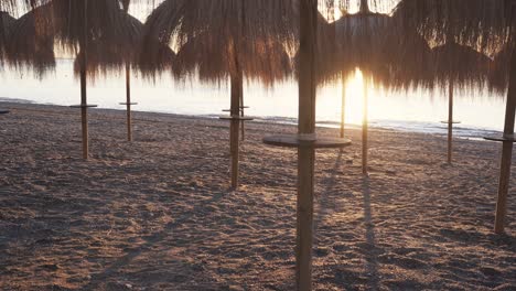 slow pan right at marbella beach during sunrise with beautiful tiki straw sun umbrellas on beach, bright sunrise giving warm look and feel to 4k footage