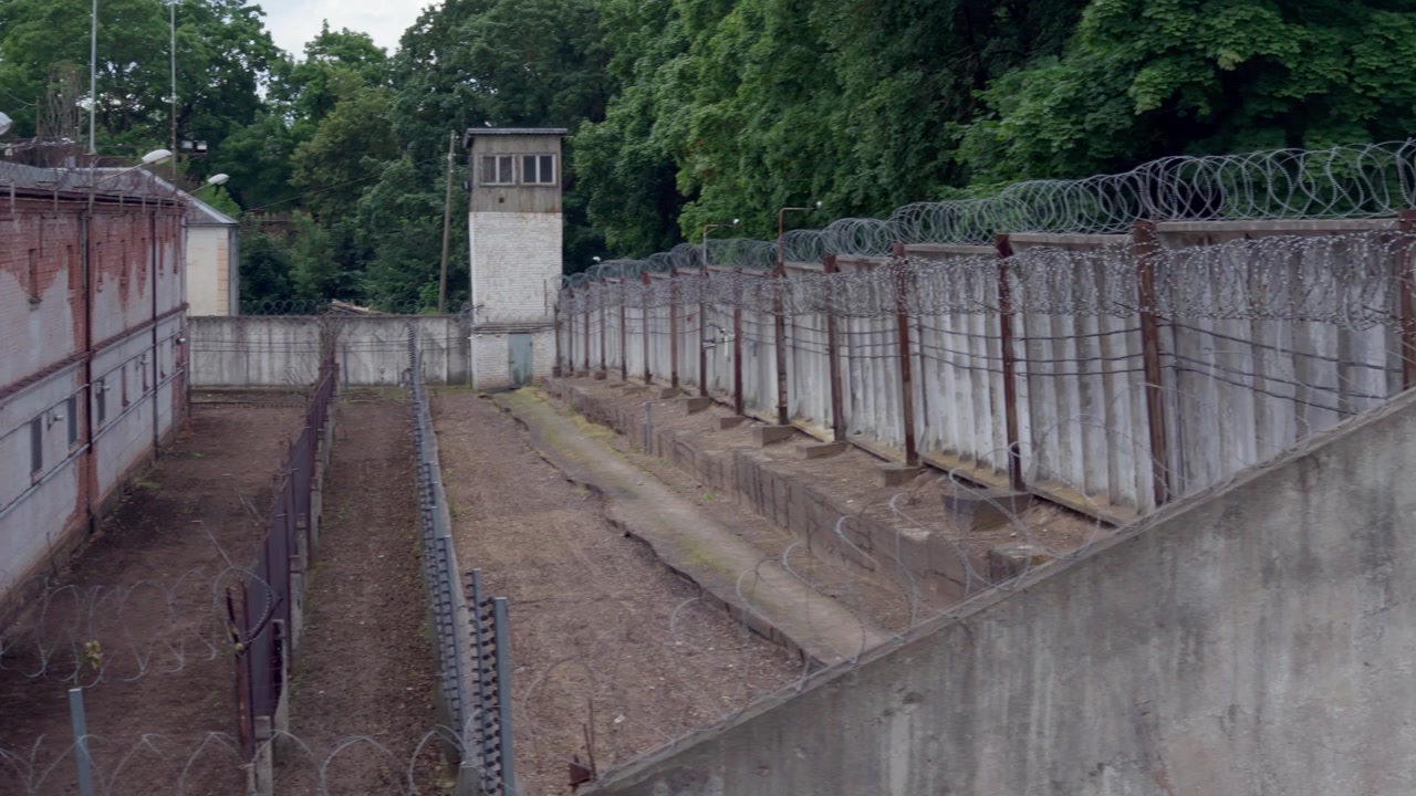 Amplio movimiento panorámico de cámara mostrando la esquina de un muro de hormigón con luminaria y alambre de seguridad enrollado en una instalación penitenciaria histórica en la ciudad de Daugavpils