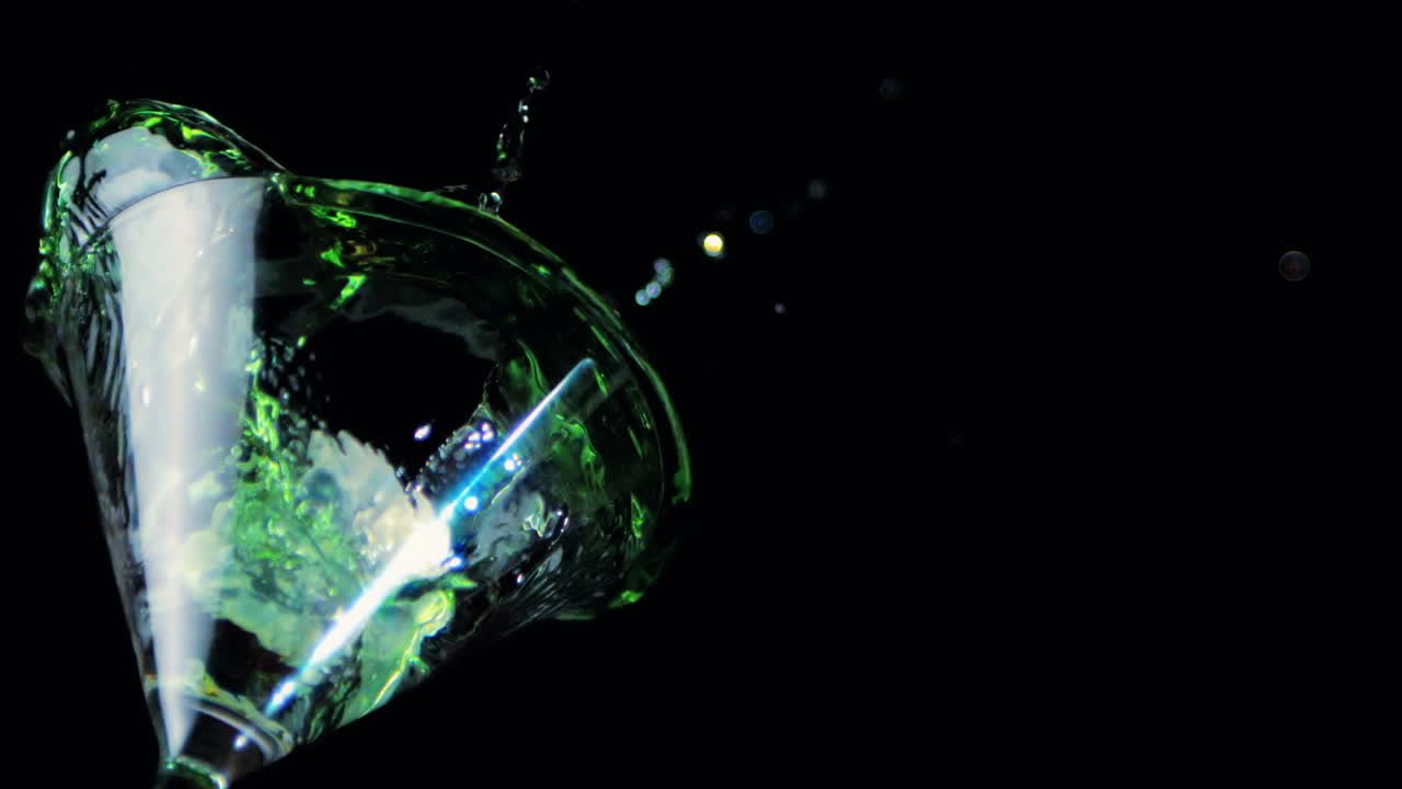 Ghiaccio che cade in un bicchiere da cocktail con liquido verde